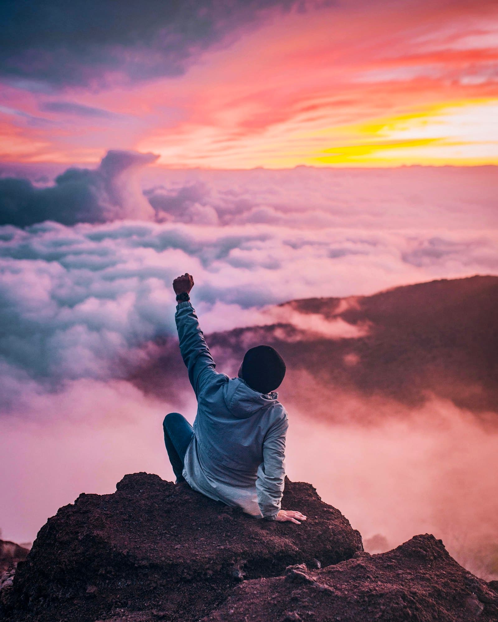 Person resting on a hilltop above the clouds at golden hour