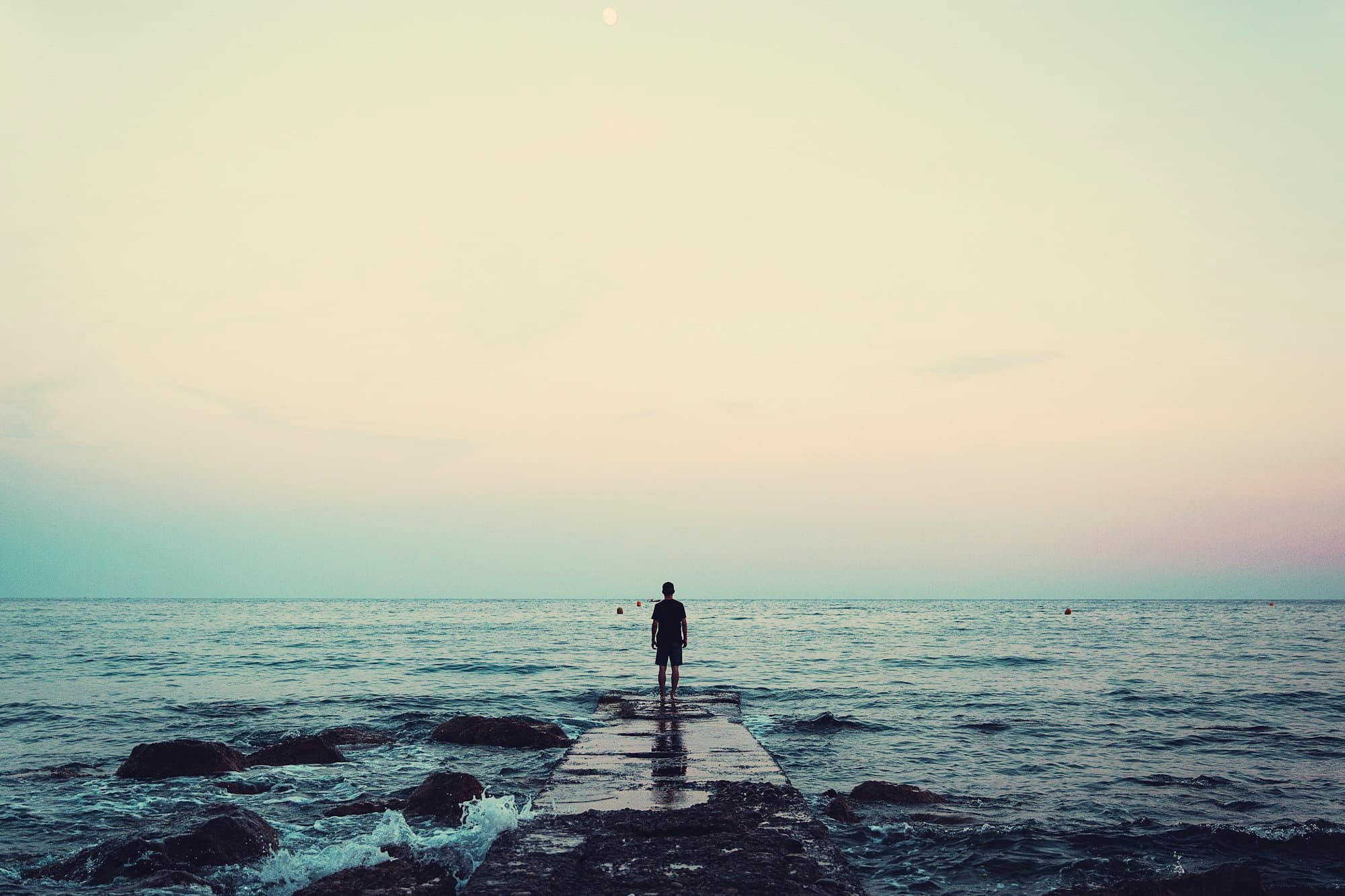 Person standing quietly on a sea dock beneath a cloudy sky