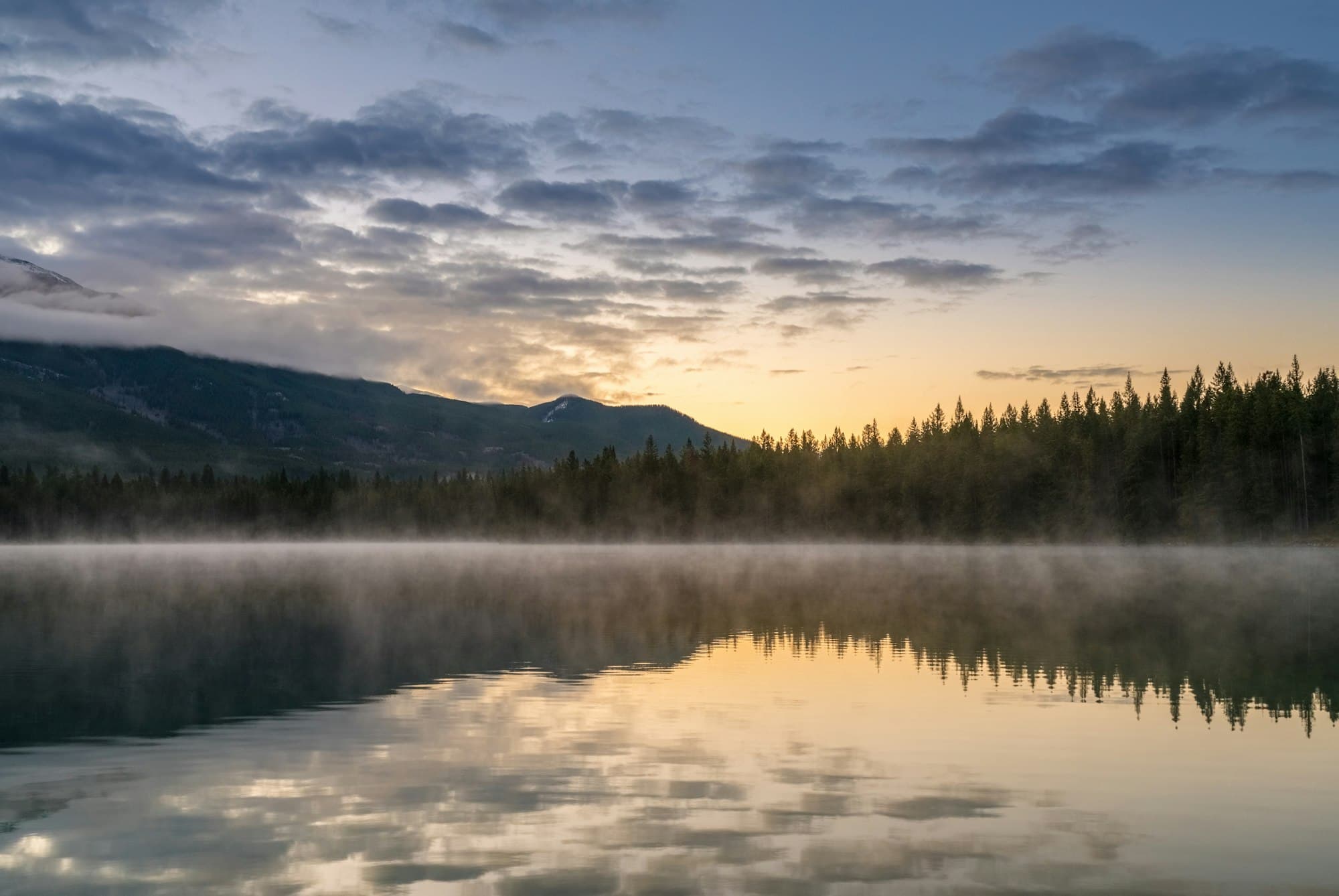 Misty lake at sunrise reflecting mountains and forest